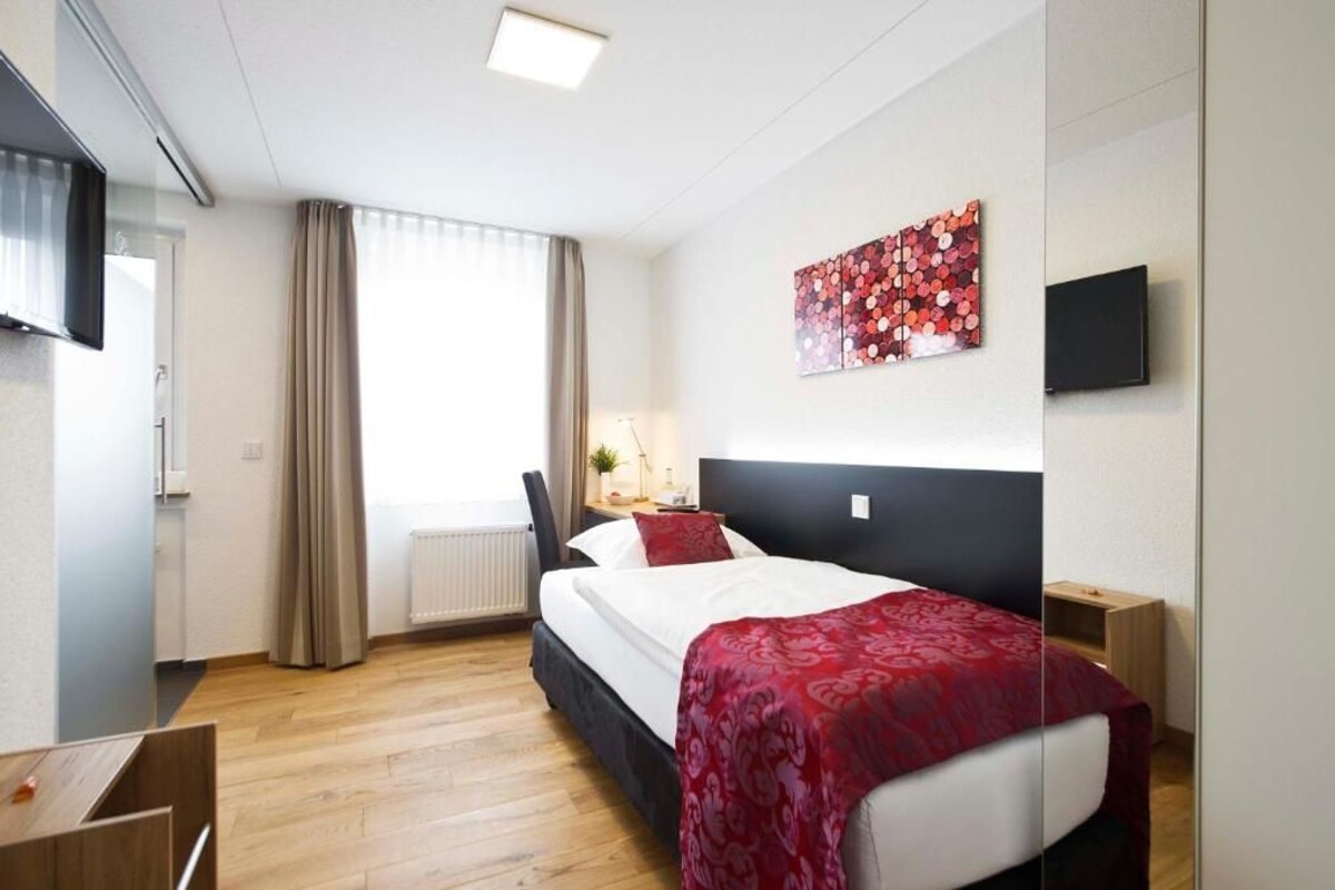 Habitación de hotel con cama, escritorio, silla, televisor y ventana con cortinas.