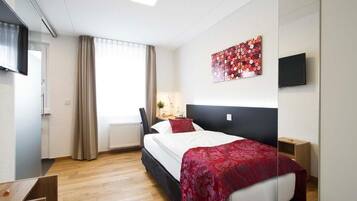 A hotel room with a bed, a desk, a chair, a TV, and a window with curtains.