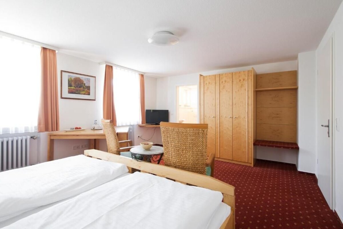 Una habitación de hotel con una cama, un escritorio con una silla, un televisor y un armario.