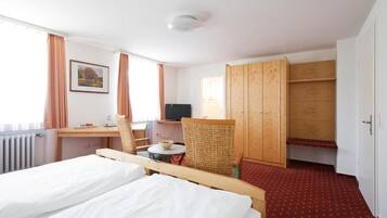 A hotel room with a bed, a desk with a chair, a television, and a wardrobe.