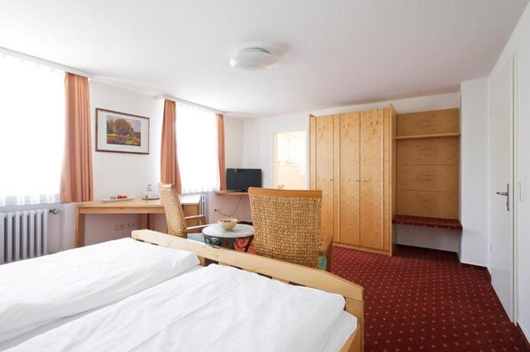 Una habitación de hotel con una cama, un escritorio con una silla, un televisor y un armario.
