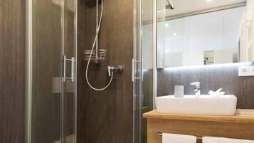 A modern bathroom with a glass-enclosed shower, a wooden vanity, and a white toilet.