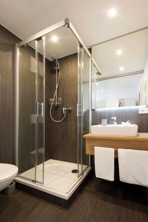 Un baño moderno con ducha envuelta en vidrio, tocador de madera y un inodoro blanco.