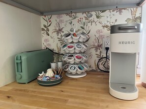 Una kitchenette con un tostador verde, una cafetera y un portavasos con diferentes cápsulas de café.