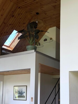 A room with a sloped wooden ceiling, a skylight, a potted plant, a framed picture, and a staircase.