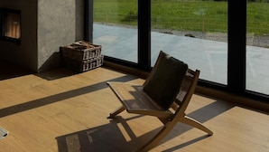 Ein Zimmer mit großen Fenstern, einem Kamin und Blick auf eine bewaldete Landschaft.