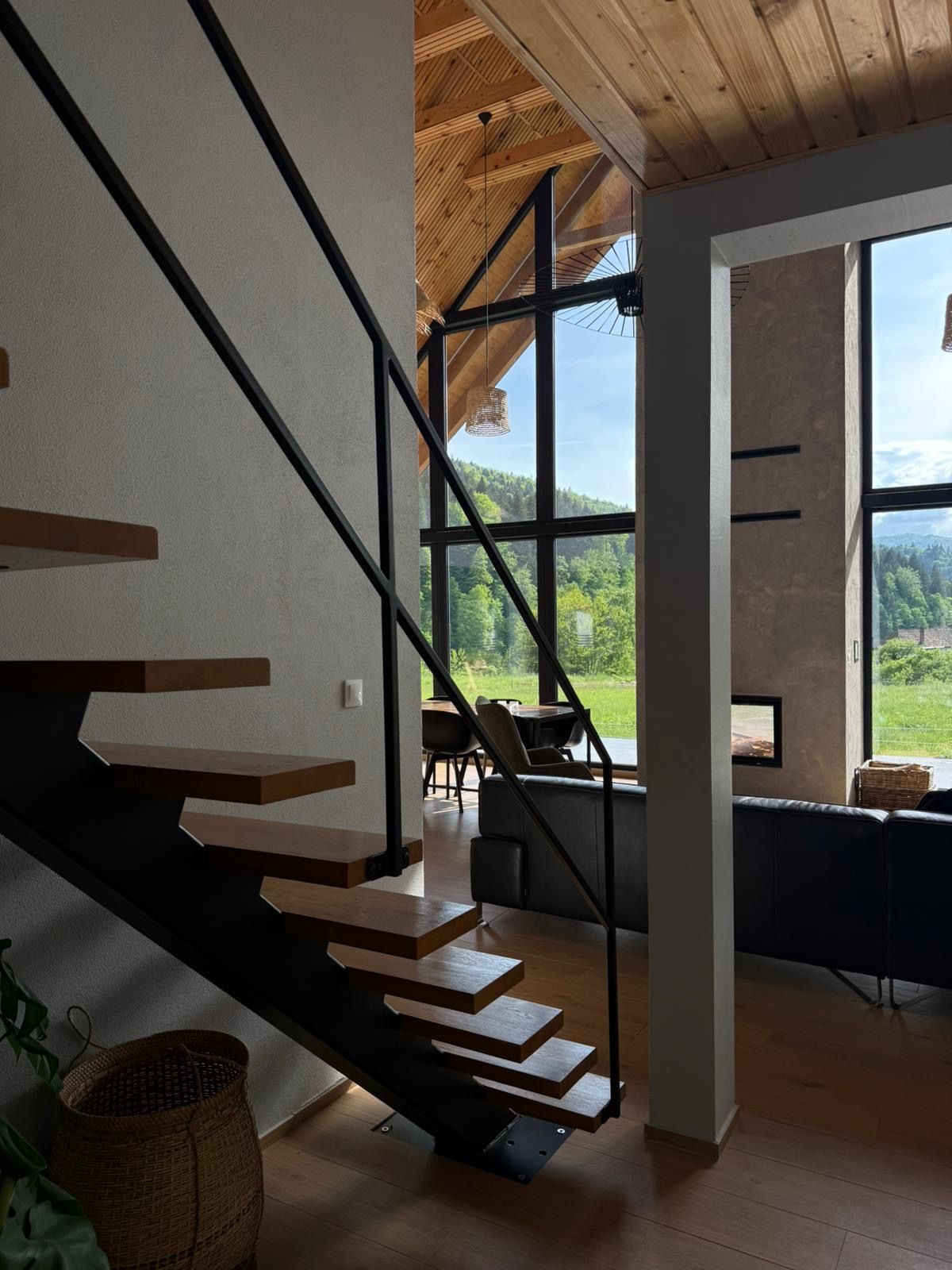 A modern interior with a staircase leading to a balcony overlooking a forested area.