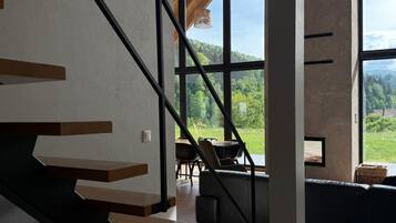 A modern interior with a staircase leading to a balcony overlooking a forested area.