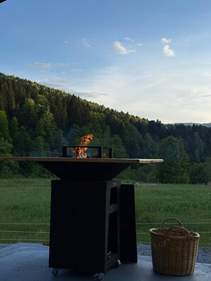 A portable grill with a fire burning on it, placed on a concrete surface with a basket nearby.