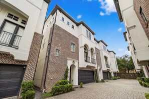 A residential building with a brick facade, multiple garage doors, and a paved driveway. - Luxury Tesla Townhouse - Medical Center (Houston)