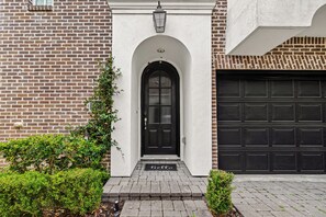 A brick house with a black front door, a garage door, and a small garden area. - Luxury Tesla Townhouse - Medical Center (Houston)