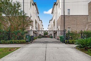 A gated residential area with a paved walkway leading to a row of brick buildings. - Luxury Tesla Townhouse - Medical Center (Houston)
