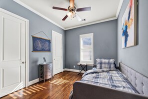 A bedroom with a bed, a ceiling fan, a window with blinds, a door, and a wall-mounted artwork. - Luxury Tesla Townhouse - Medical Center (Houston)