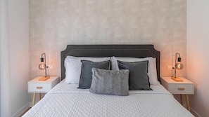 A neatly made bed with a white duvet, two bedside tables with lamps, and a patterned wall. - Villa Turística Palomas Torrox by Ruralidays (Málaga)