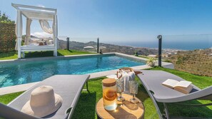 A poolside area with a pergola, lounge chairs, and a table with drinks and a book. - Villa Turística Palomas Torrox by Ruralidays (Málaga)