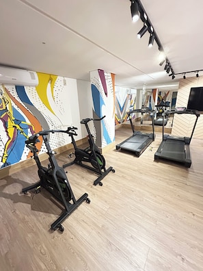 Ein Fitnessraum mit Trainingsgeräten, darunter Fahrrädern und Laufbändern, sowie einer Spiegelwand.