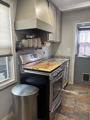 A kitchen with a stainless steel stove, oven, and a trash can.