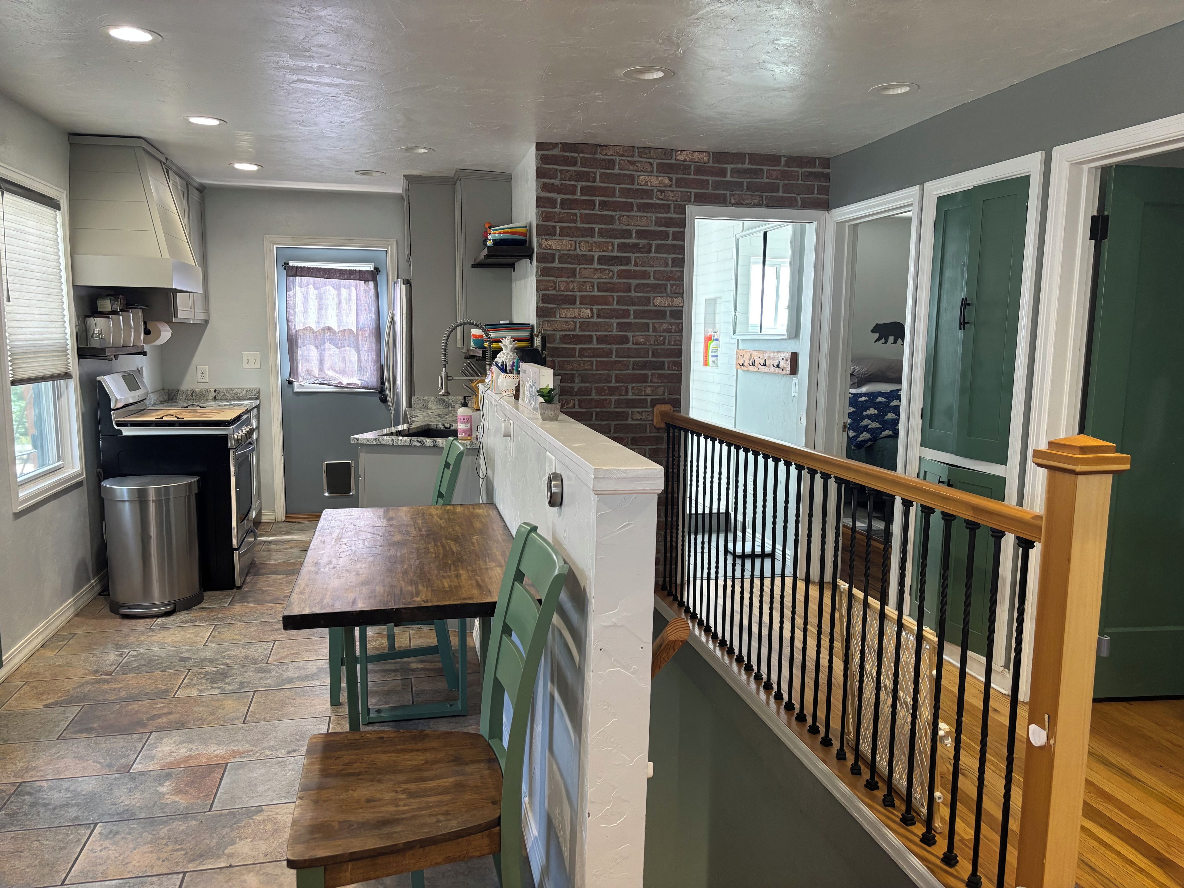 A compact kitchen with a dining area, a trash bin, and a staircase leading to a green door.