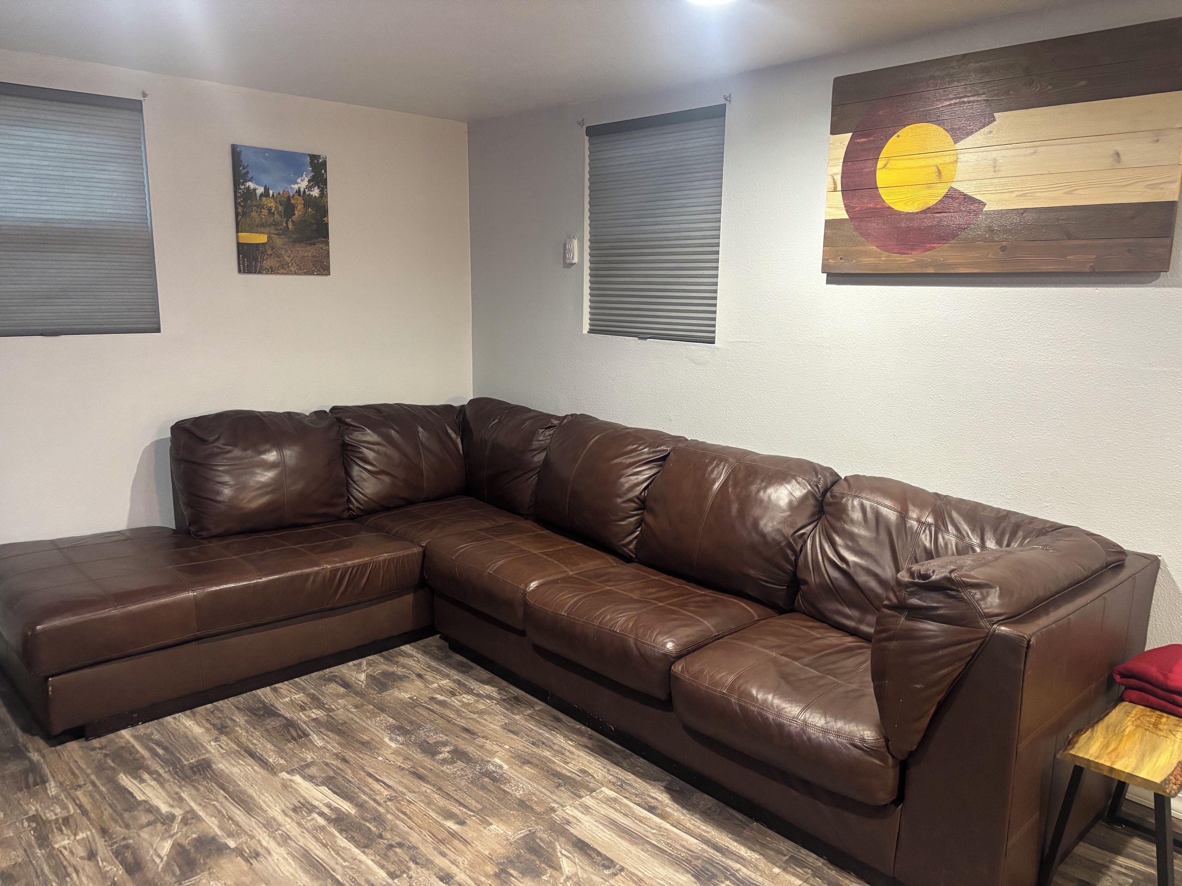A brown leather sectional sofa in a room with a wooden floor, a painting of a landscape, and a wall-mounted artwork.