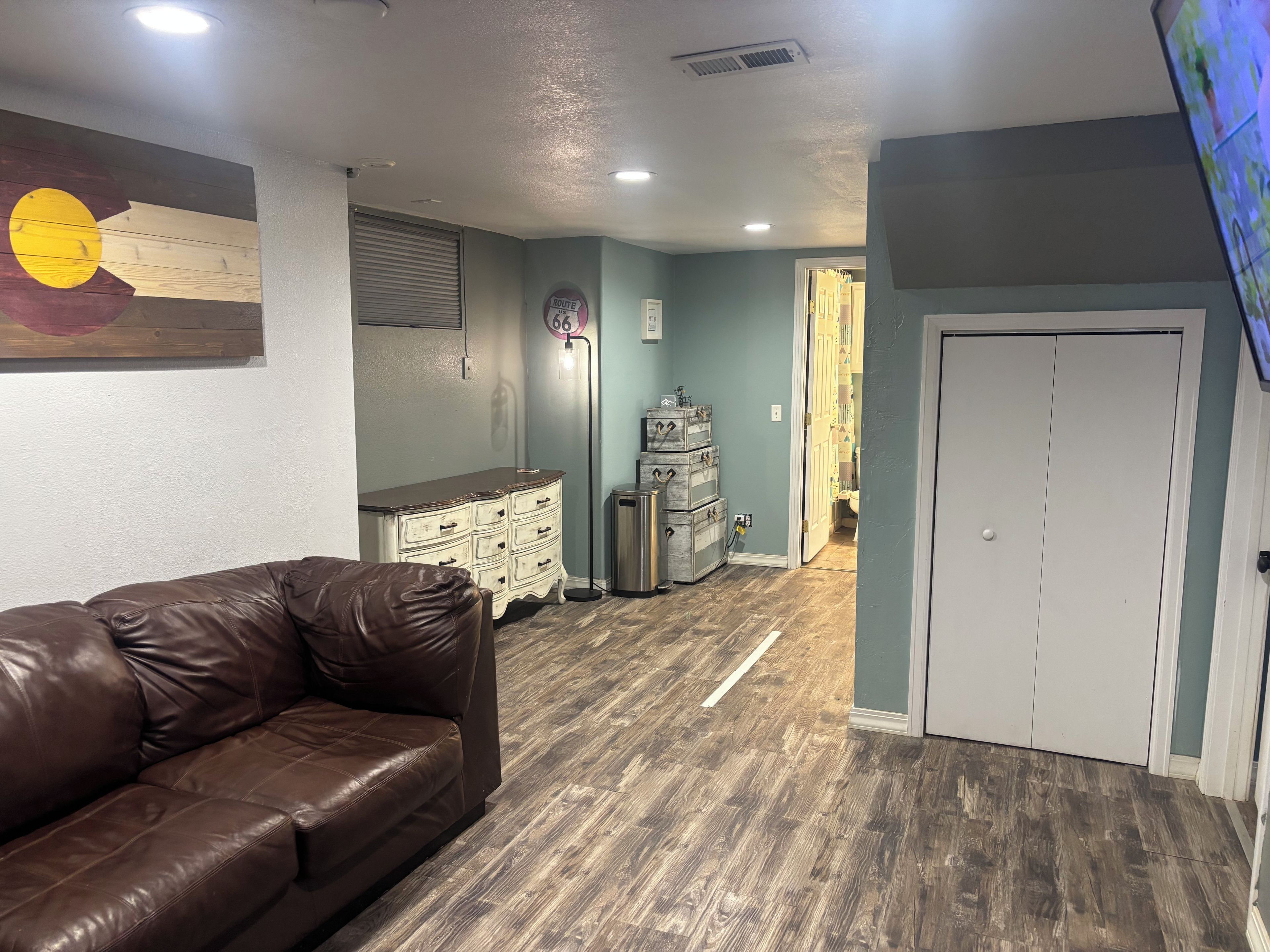 A room with a brown leather couch, a wall-mounted artwork, a wooden cabinet, and a door leading to another room.