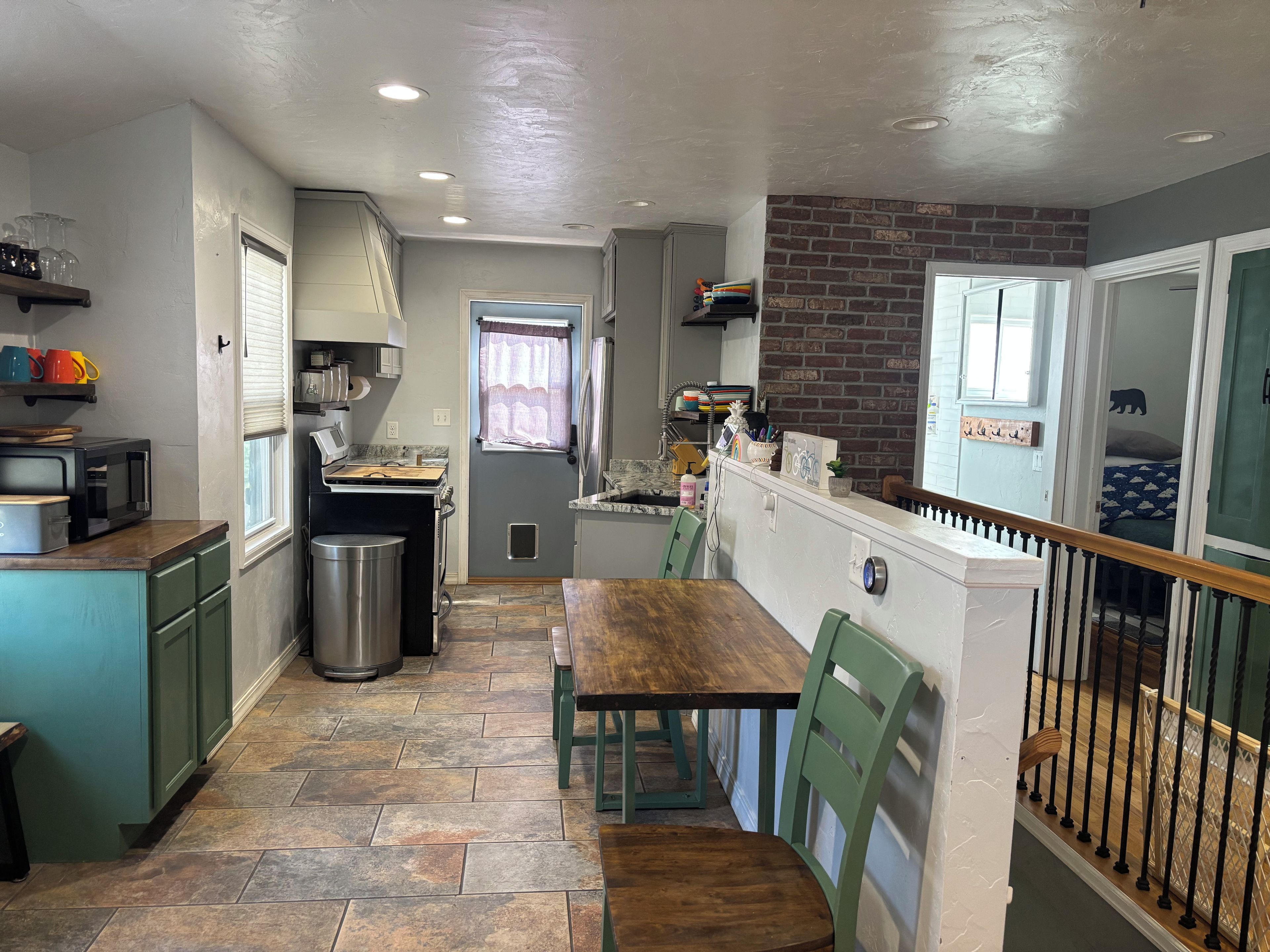 A compact kitchen with a dining area, a trash bin, and a window with curtains.
