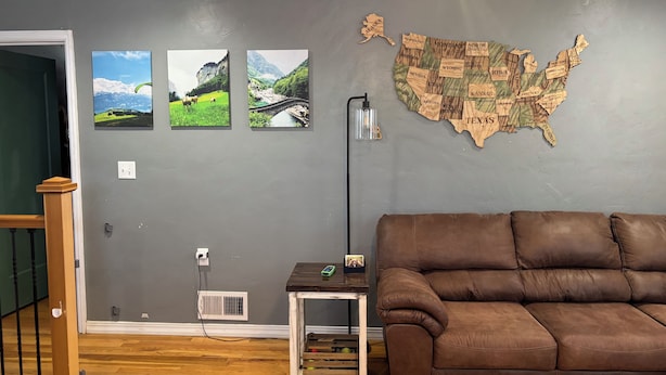 Una sala de estar con un sofá de cuero marrón, un mapa de los Estados Unidos colgado en la pared y tres fotografías enmarcadas de paisajes.