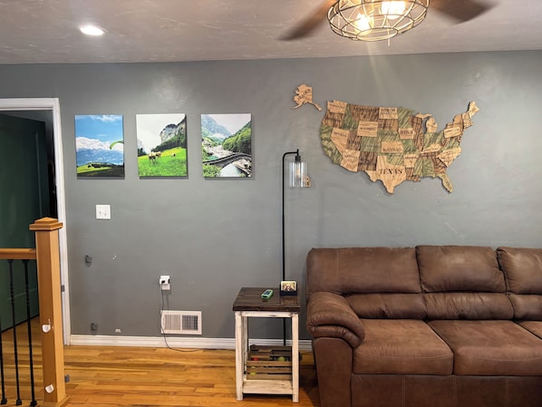 Un salon avec un canapé en cuir marron, une carte des États-Unis accrochée au mur et trois photographies de paysages encadrées.