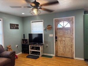 A room with a ceiling fan, a mounted TV, a wooden door, and a shoe rack.