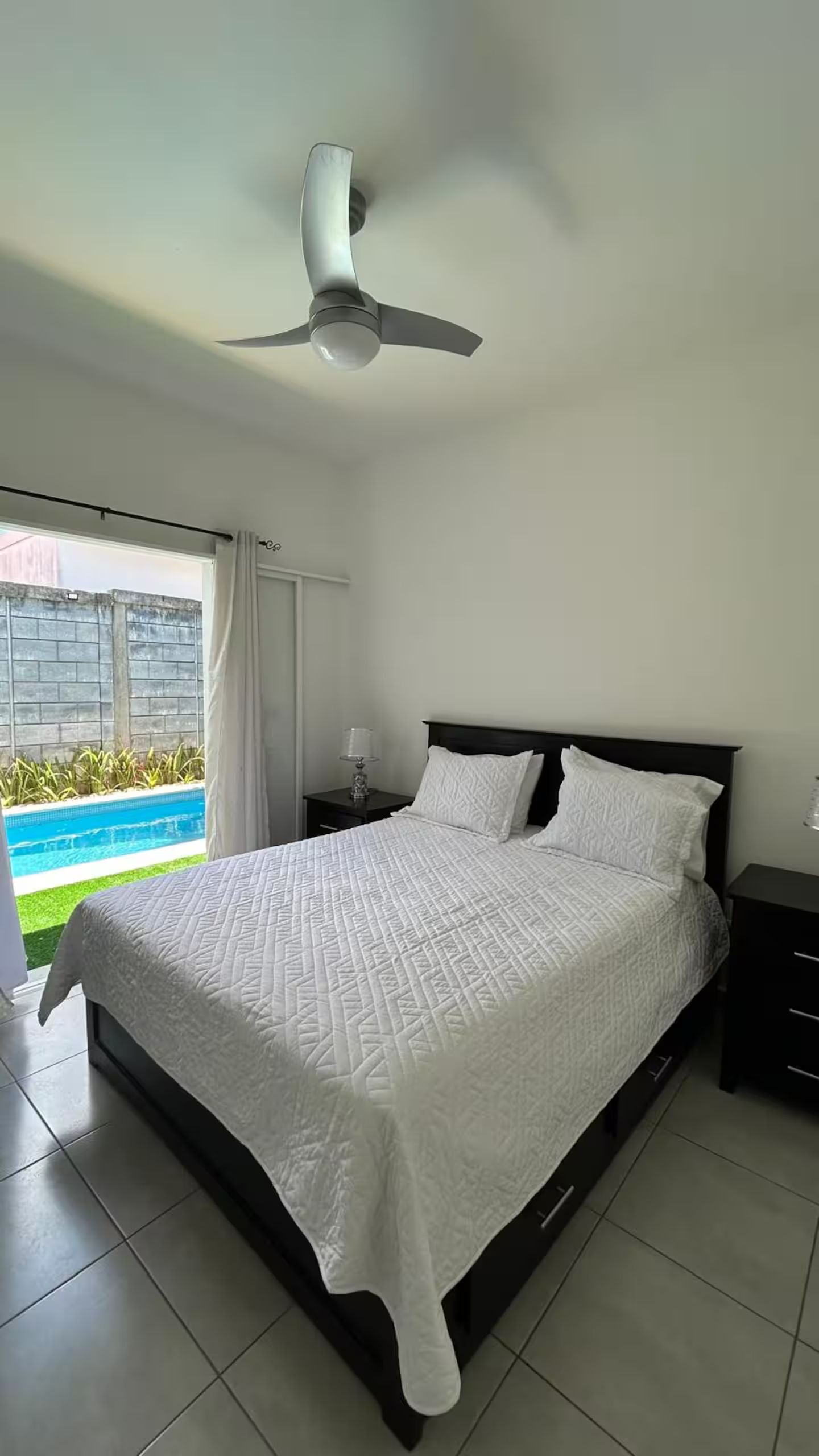 Ein Schlafzimmer mit einem Bett, einem Nachttisch, einer Lampe und einem Deckenventilator.