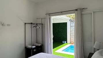 A bedroom with a bed, a ceiling fan, a nightstand, a hanging light, and a view of a swimming pool through an open door.