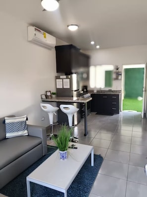 A modern living room with a sofa, a coffee table, and a kitchen area with a refrigerator, stove, and bar stools.