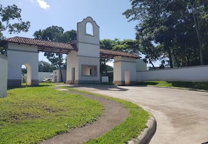 A building with a central tower and arched openings, surrounded by a paved area and greenery.