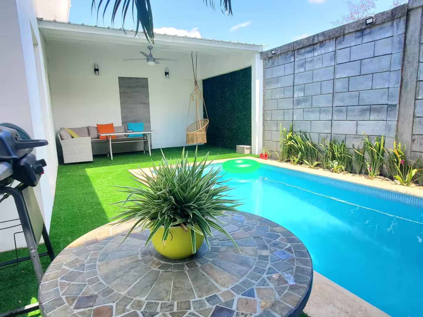 Piscina com borda em azulejo, mesa redonda de pedra e cadeira suspensa.