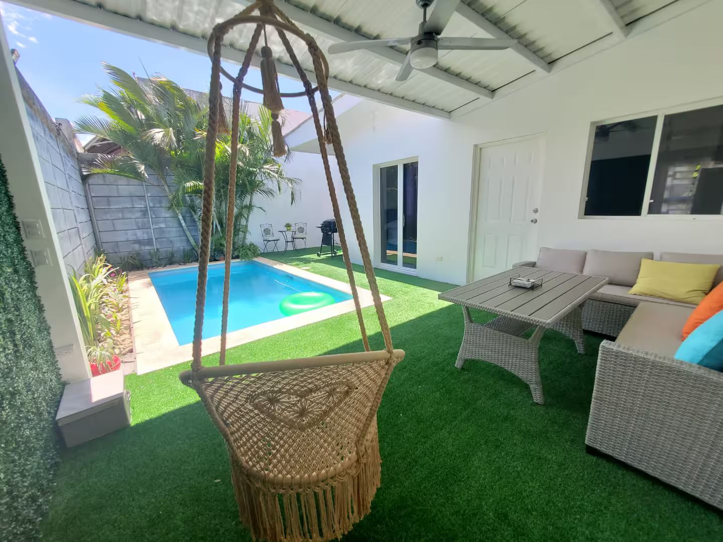 Un espacio al aire libre techado con piscina, mobiliario de mimbre y una silla colgante.