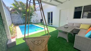 Un espacio al aire libre techado con piscina, mobiliario de mimbre y una silla colgante.