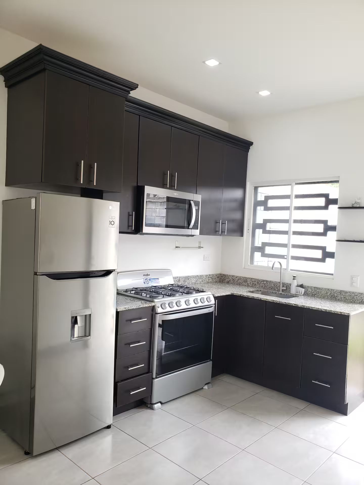 A modern kitchen with dark cabinets, stainless steel appliances, and a granite countertop.