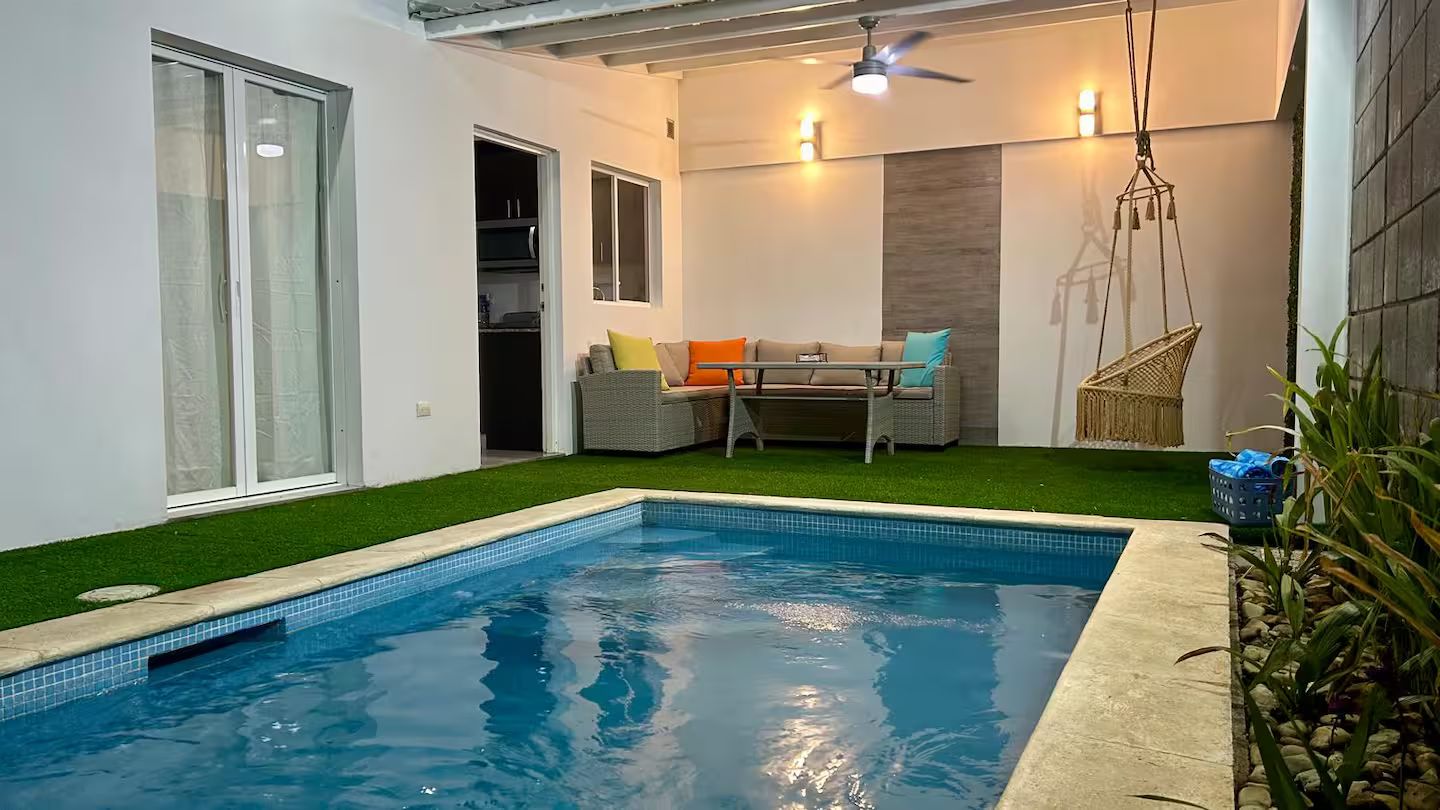 Una piscina con cerramiento de vidrio, un área de descanso con mesa y sillas, y un ventilador de techo.