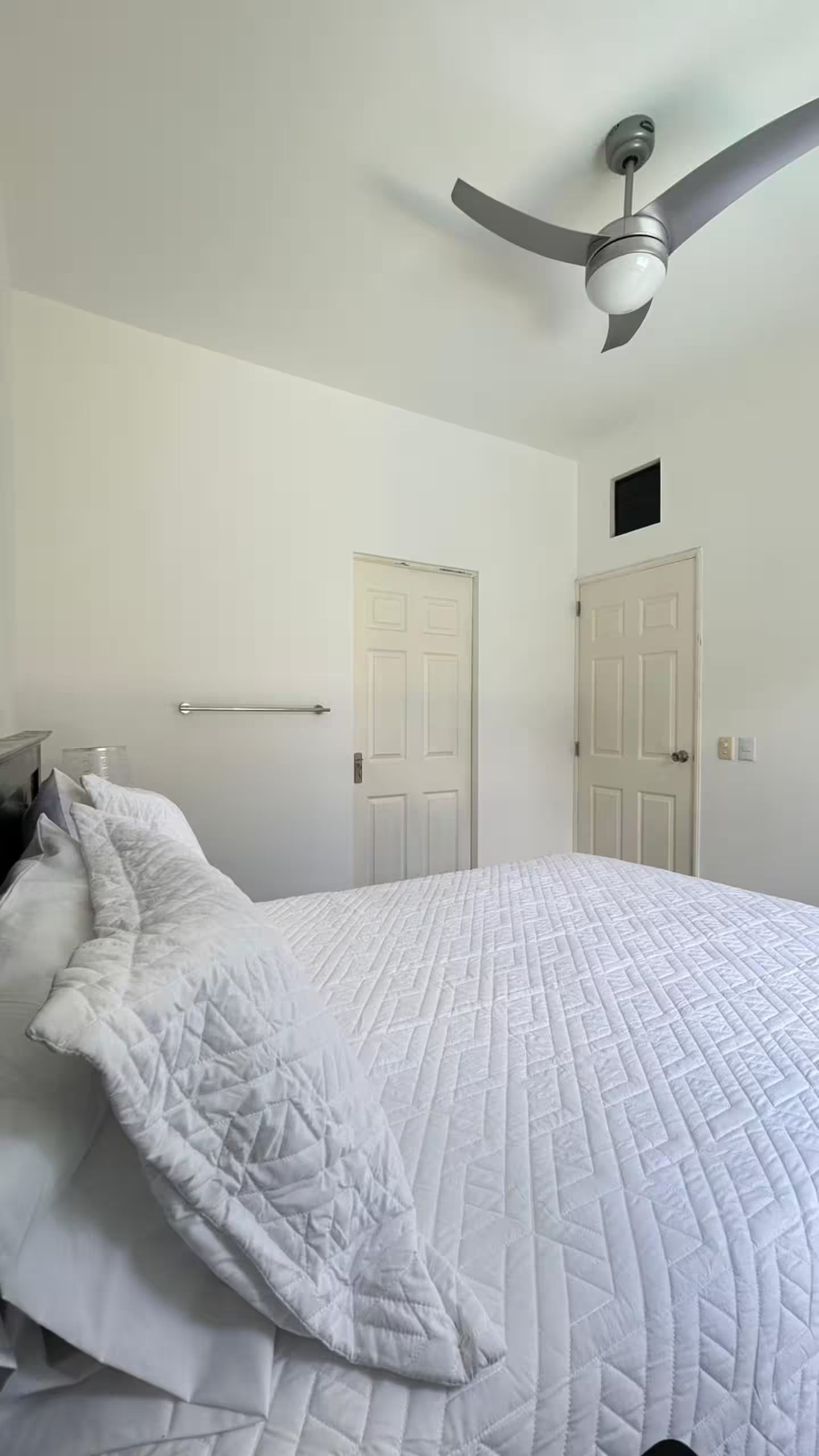 Quarto com cama, duas portas, ventilador de teto e mesa de cabeceira.