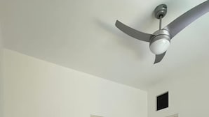 A bedroom with a bed, two doors, a ceiling fan, and a nightstand.