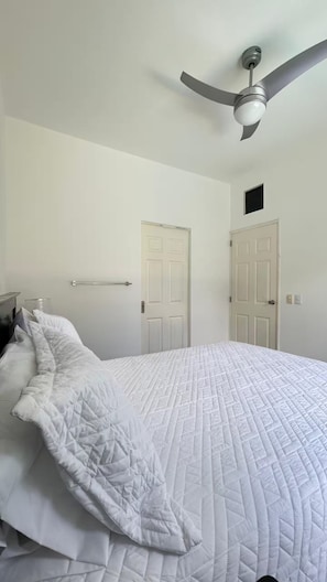 A bedroom with a bed, two doors, a ceiling fan, and a nightstand.