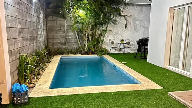 A rectangular pool with a tiled edge, surrounded by artificial grass, with a concrete wall on one side and a white wall on the other.