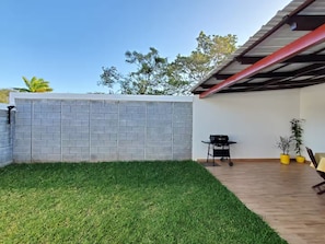 A backyard with a brick wall, a grassy area, a barbecue grill, and potted plants.