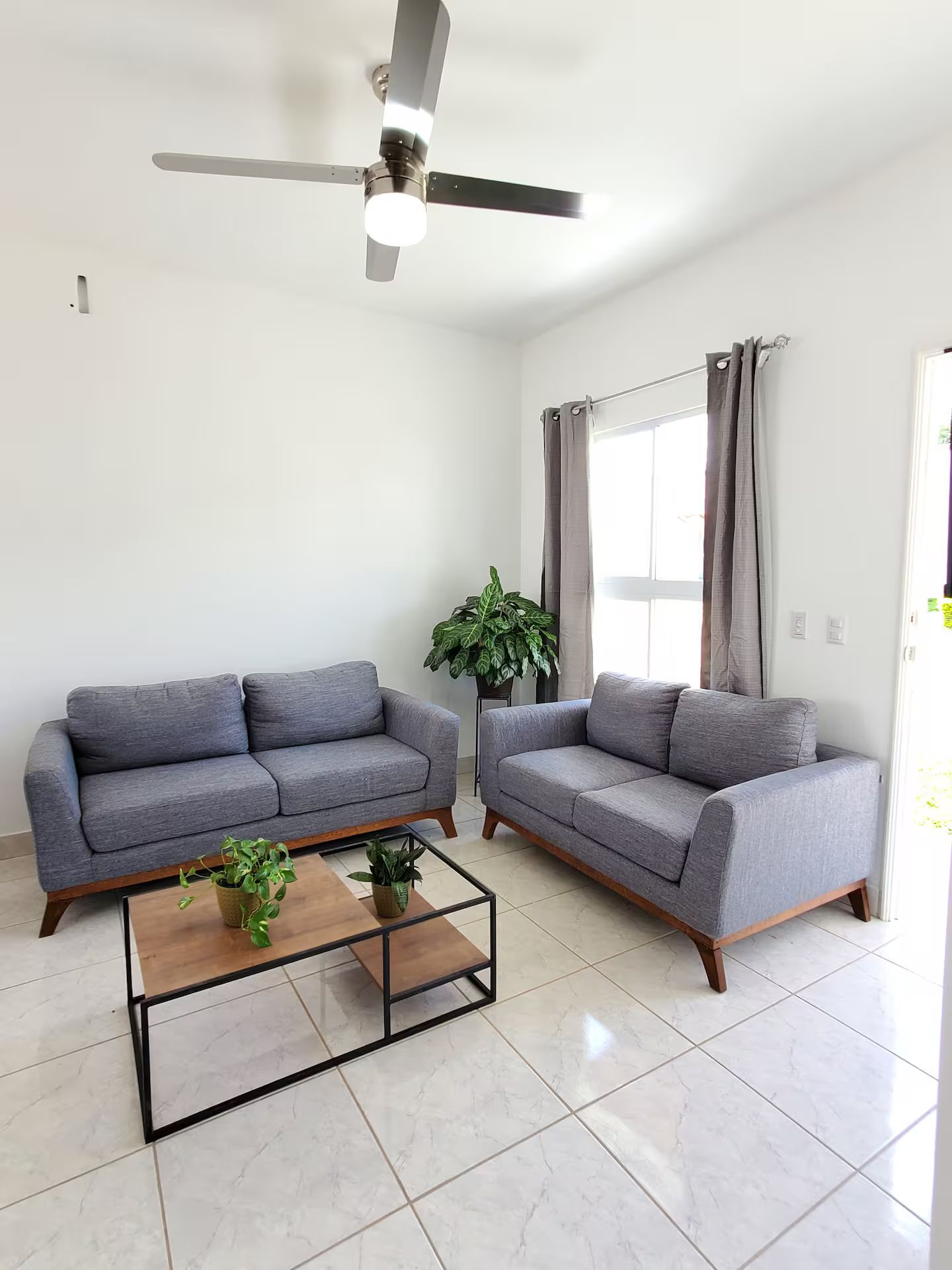 Un salon moderne avec deux canapés gris, une table basse en bois et un ventilateur de plafond.