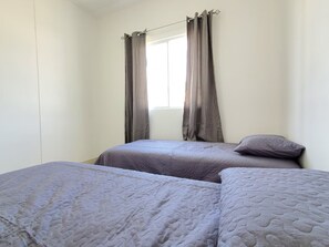 A bedroom with two beds, a window with curtains, and a plain wall.