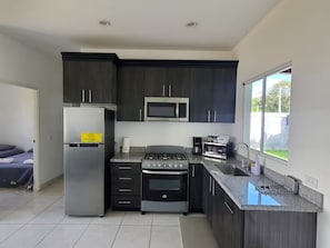 Una cocina moderna con muebles oscuros, electrodomésticos de acero inoxidable y un amplio ventanal que proporciona luz natural.