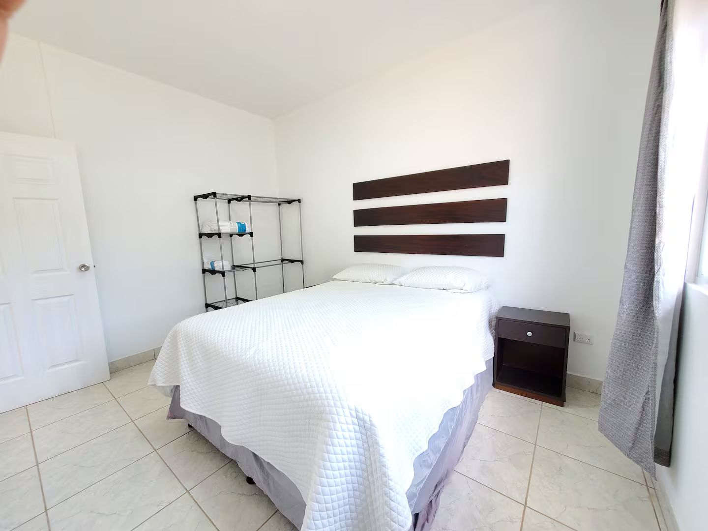 Ein Schlafzimmer mit einem Bett, einem Metallschrank, einem Nachttisch und einer Tür.