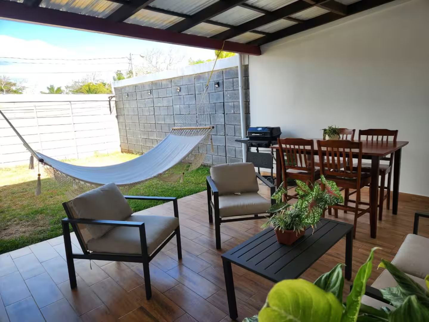Un patio con hamaca, sillas, una mesa y una planta en maceta.