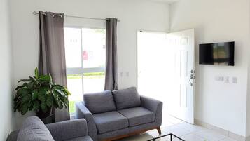 A modern living room with a grey sectional sofa, a coffee table, a ceiling fan, and a TV mounted on the wall.