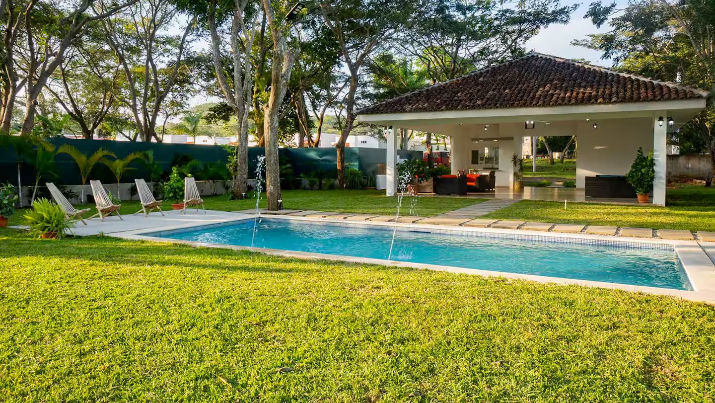 Piscina com espreguiçadeiras, área de estar coberta e gramado bem cuidado.