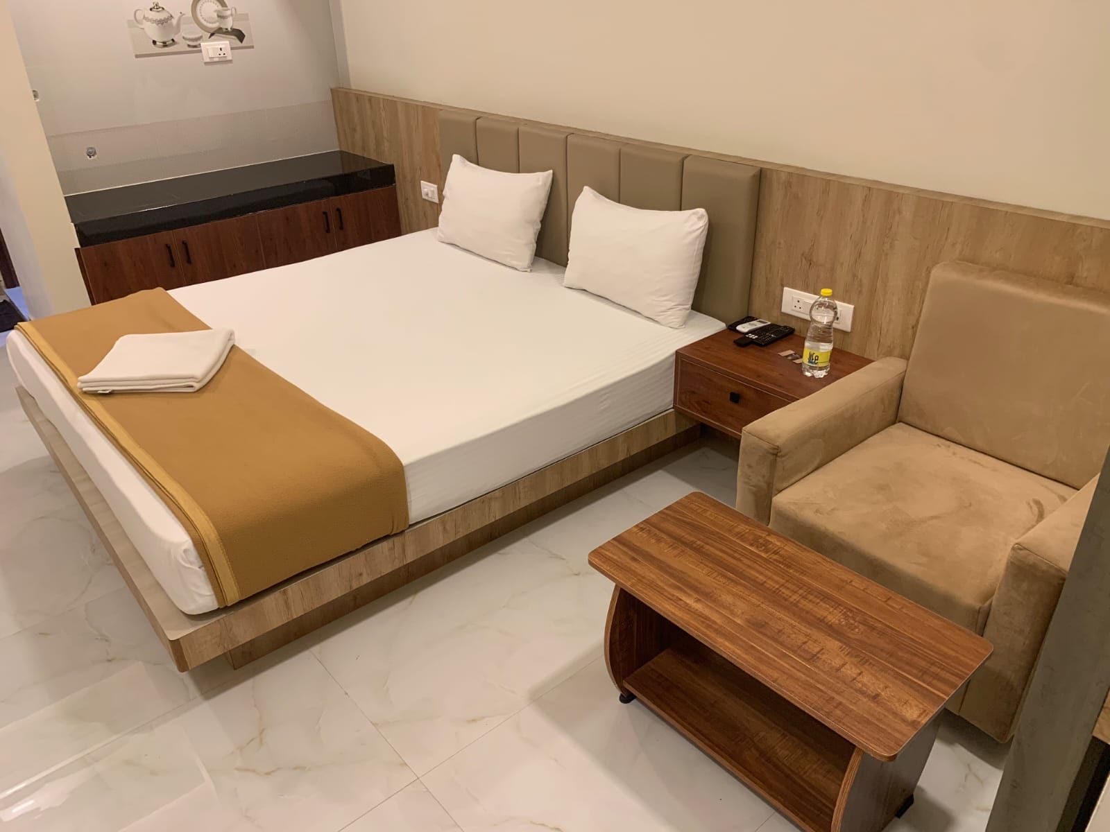 A hotel room with a bed, a bedside table, a chair, and a small wooden table.